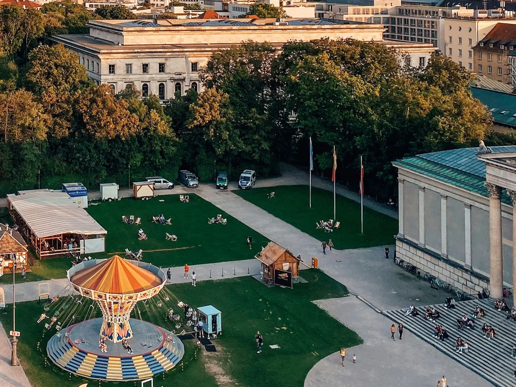 Menschen in München sitzen auf Treppenstufen vor einem Gebäude, fahren Kettenkarussell oder sitzen in Liegestühlen auf einer Wiese