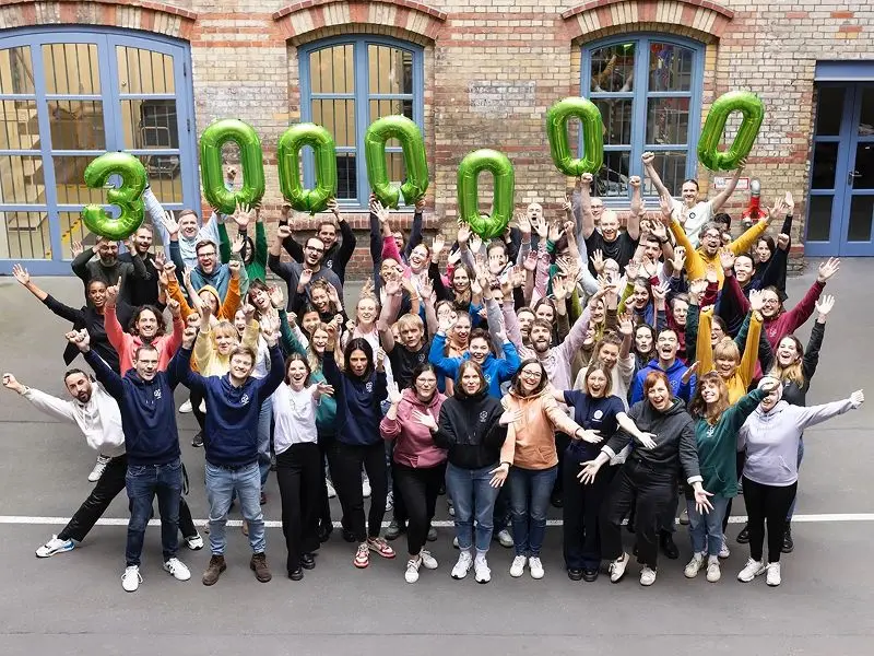 Das nebenan.de-Team steht gemeinsam im Hof und hält bunte Luftballons mit Ziffern in die Höhe, die zusammen die Zahl ‚3 000 000‘ ergeben, um drei Millionen Nutzer zu feiern.